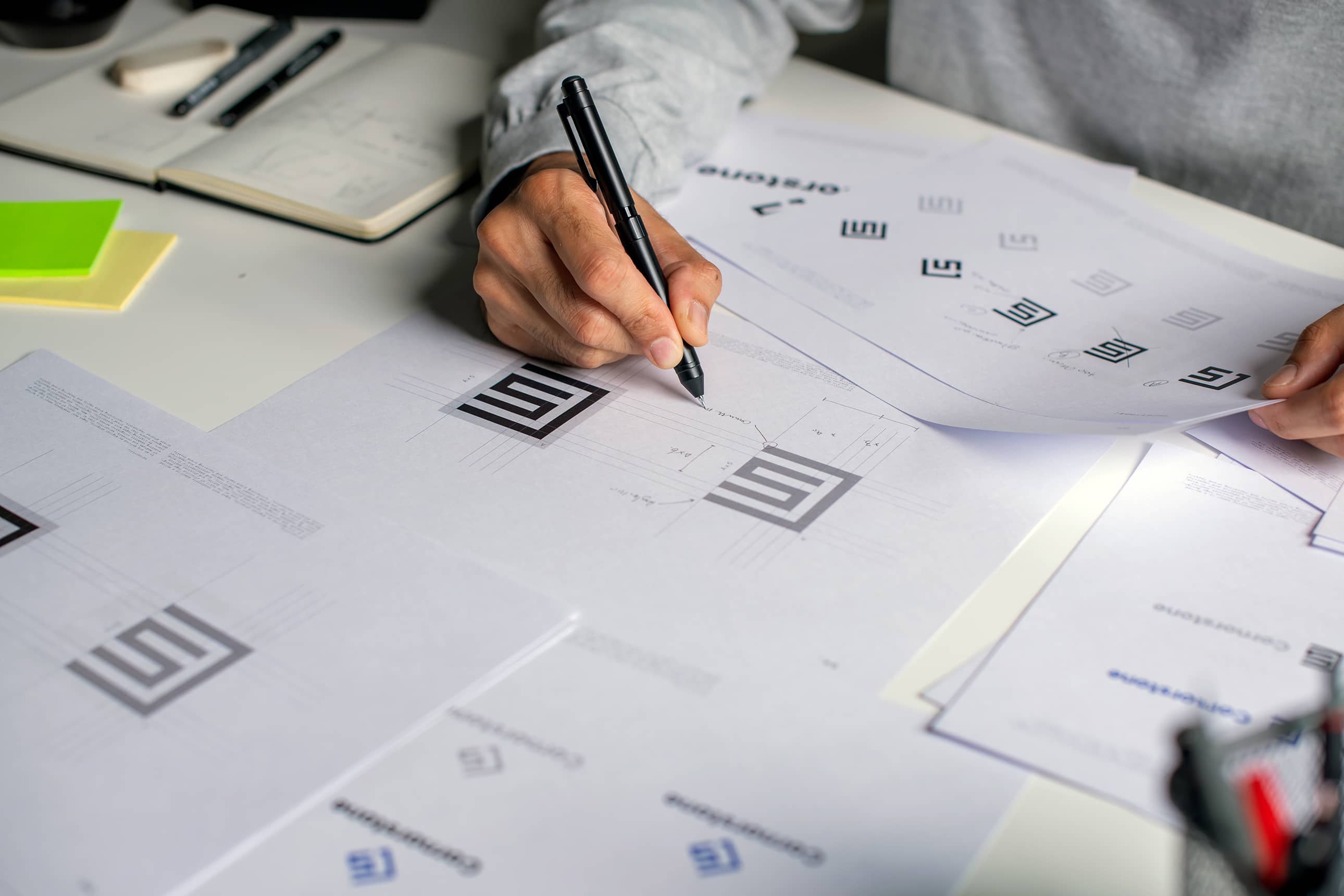 Χέρια σε γραφείο που εργάζονται σε σχέδια brand, λογότυπα και στρατηγική οπτικής ταυτότητας