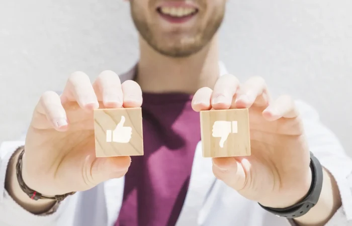 Νέος άνδρας με λευκό ιατρικό μανδύα κρατά ξύλινα blocks thumbs up και thumbs down, συμβολίζοντας ιατρική εγκρίνει και απόρριψη