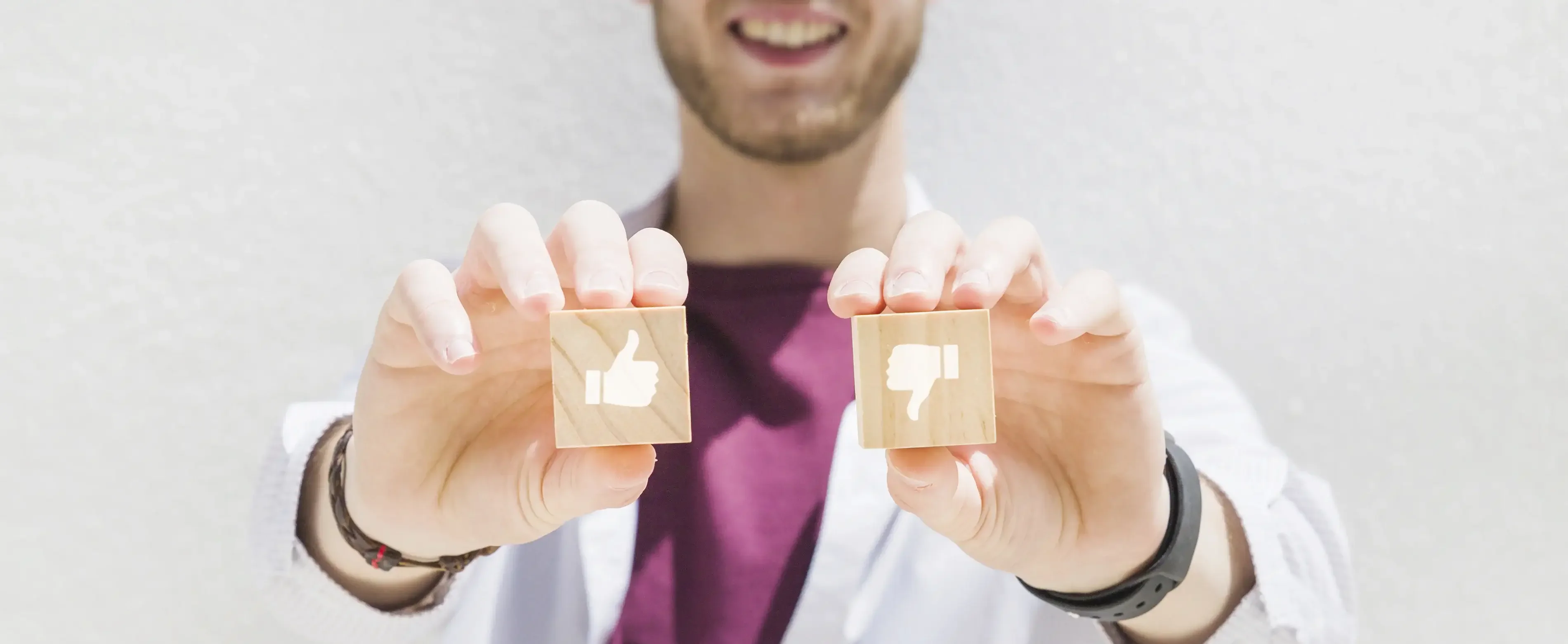 Νέος άνδρας με λευκό ιατρικό μανδύα κρατά ξύλινα blocks thumbs up και thumbs down, συμβολίζοντας ιατρική εγκρίνει και απόρριψη